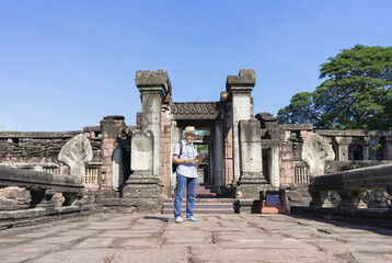 senior man with grey hair and beard,wearing hat,carry backpack and having camera, searching data on tablet at Phimai historical park,Thailand. concept ancient tourist, ecotourism, archeologist - obrazy, fototapety, plakaty