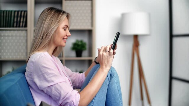 Happy woman chatting smartphone dating online application relaxing home cozy interior closeup
