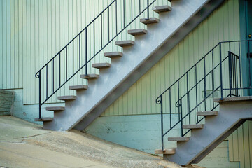 Top and bottom stair case with metal hand rails and cement steps on slanted street on side of beige stucco building in urban city