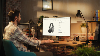 Portrait of a Handsome Bearded Young Adult Man in Casual Clothes Using Desktop Computer in Stylish Loft Apartment at Home. Happy Sound Specialist Online Shopping for Equipment and Heqdphones