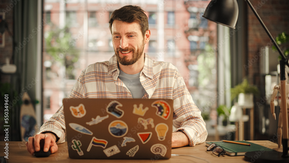 Poster creative bearded man working on laptop computer while sitting at a table in stylish cozy loft living