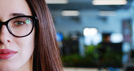 Close up of half of beautiful female face in coworking space. Attractive pretty woman in glasses in office interior. Portrait shot. White-collar worker employee.