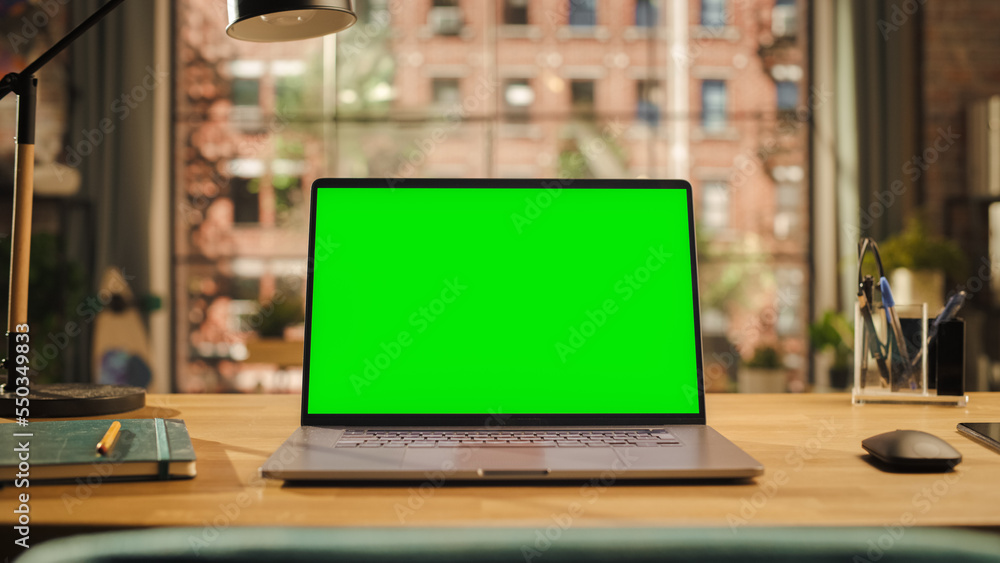 Poster laptop computer display with mock up green screen standing on a wooden desk in living room. chroma k