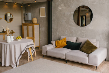 Cozy Scandinavian style interior of the living room with a gray sofa with pillows, a round dining table in a country house