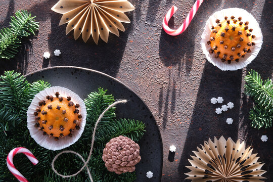 Wintertime dark background with fragrant pomander balls. Classical decorations - tangerine with cloves. Handmade paper stars from brown baking paper, pine cones, fir twigs and burning beewax candle.