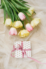 Beautiful spring bouquet of pink and yellow tulips and a gift with a ribbon on a beige background. Flat lay and copy space