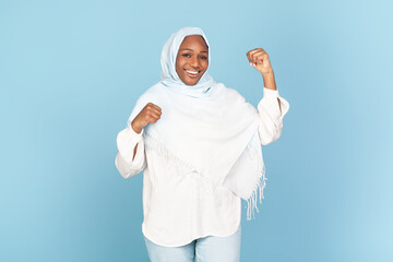 Great bonus. Excited african american muslim lady in headscarf celebrating success, shaking fists and smiling at camera