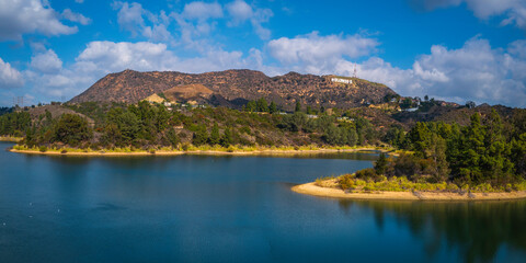Hollywood Reservoir, Hollywood sign in the background, a tranquil natural park landscape with seagulls in the water and dramatic clouds in the blue sky, in Los Angeles, California  