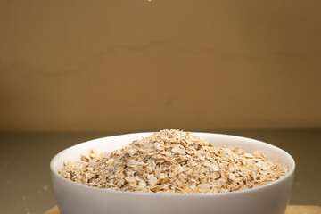 Avena molida siendo vertida en un bol blanco con una cuchara de metal en un fondo aislado. Bol repleto de avena. Plato hondo blanco con avena molida. Plato blanco de cerámica. 