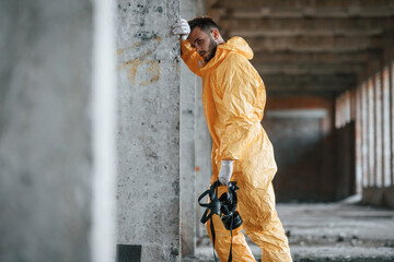 Tired, frightened. Leaning on the wall. Man dressed in chemical protection suit in the ruins of the...