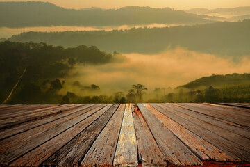 An empty wooden terrace with mountain view and mist during sunrise.	