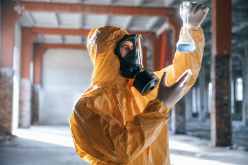 A test tube with radioactive materials. Man dressed in chemical protection suit in the ruins of the...