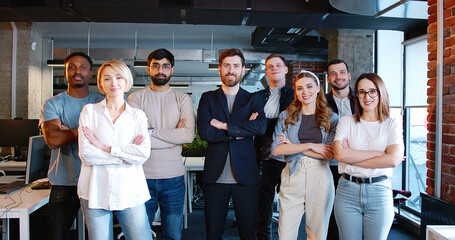 Portrait of multiethnic business team standing in office smiling to camera and crossing hands. Diverse coworkers. Young men and women, coworkers of IT startup. Business colleagues. Management strategy