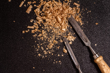 two wooden-handle chisel with wooden chips and sawdust on a black speckled background top view