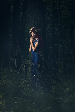 Vertical portrait of a Caucasian woman in a blue dress posing in a forest