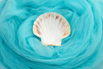Sea shell on turquoise blue fabric texture. Backdrop for product placement.