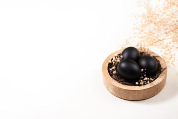 Eggs painted black on white background. Nest containing three egg with beautiful gypsophila flowers. Minimal Easter concept with copy space for text.