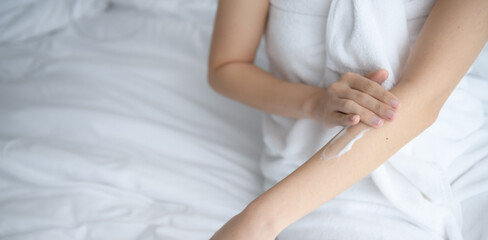 Fototapeta na wymiar Asia woman sitting on bed and applying cream on her body.
