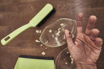 Close-up of a cut female finger on the background of a split cup and a brush with a dustpan for cleaning. A wound with blood received when cleaning broken dishes. High quality photo