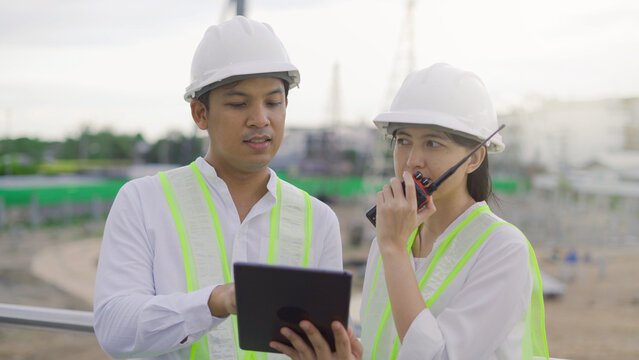 Two civil engineer work inspecting architect drawing on tablet at construction site.