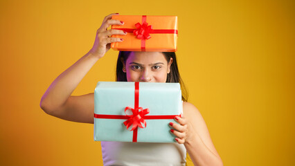 Portrait of an attractive cheerful happy girl holding gift box in hand, Young Asian Indian woman with gifts isolated over color background
