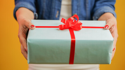 Closeup of a girl hand giving a gift box, handmade present wrapped in paper, woman with gifts isolated over color background