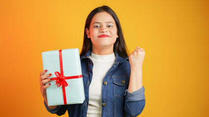 Portrait of an attractive cheerful happy girl holding gift box in hand, Young Asian Indian woman with gifts isolated over color background