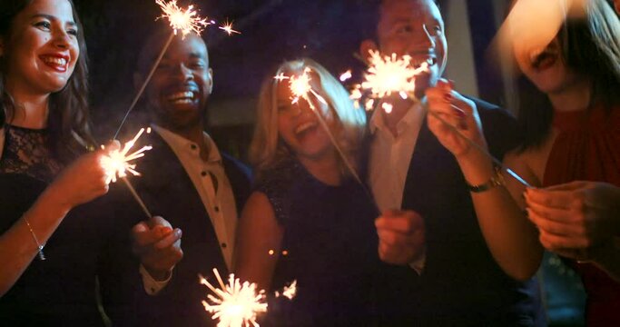 Party, sparkler and friends dance in a night celebration of a new year or happy birthday with freedom at a social event. Smile, support and excited people celebrate success or goals dancing together