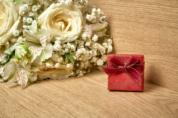 Red gift box with bow on lid, bouquet of white flowers on wooden background, holiday