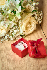 White gold ring in a red gift box, bouquet of white flowers on a wooden background, holiday