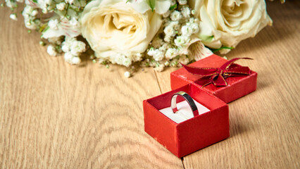 White gold ring in a red gift box, bouquet of white flowers on a wooden background, holiday