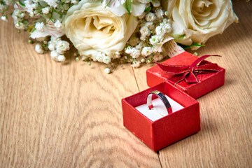 Silver ring in red gift box, bouquet of white flowers on wooden background, holiday