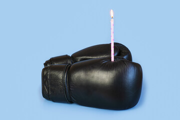 Pair of black leather boxing gloves with a burning birthday candle. Holiday greetings concept....