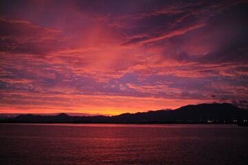 Red, pink, orange and violet sunrise at the seaside during dawn with clouds in the sky and mountains on the shore