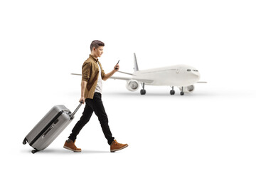 Full length profile shot of a young man with a smartphone pulling a suitcase in front of a plane