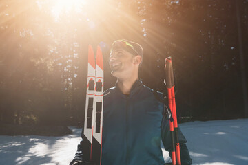 Portrait handsome male athlete with cross country skis in hands and goggles, training in snowy...