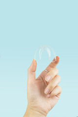 Teeth Whitening - Tooth Tray in woman hand, Close-up. Invisible removable retainers for orthodontic treatment.Invisible transparent braces on blue background. Therapy after brackets.