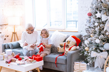 Christmas family grandmother and granddaughter sit on sofa near Christmas tree and preparing...