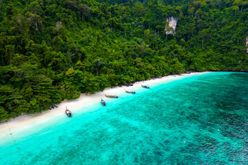 Aerial drone view of famous Monkey Beach at Ko Phi Phi island, Thailand. Tropical beach with white sand, turquoise water and green forest. Long tailed boats are waiting on beach. 