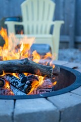 Vertical shot of a stone fire pit on a fall day with a white garden chair in the blur background - obrazy, fototapety, plakaty