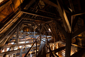 Wooden roof construction on the attic of a very old house in Sauerland Germany. Sparse light coming in from outside illuminates the dark room with timber pillars, beams and bars and balks.