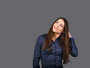 Thinking business woman in blue shirt looking up on grey background with empty copy space for text. Closeup