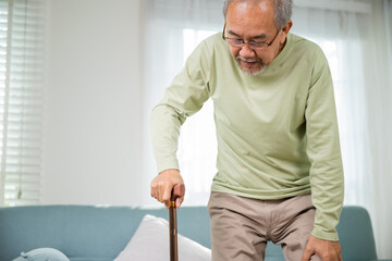 Asian Old man with eyeglasses typing to stand up from sofa with walking cane, Elderly suffering...