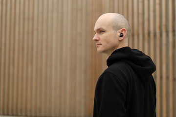Young bald man with freckles on face. Guy wearing in black hoodie and with wireless headphones....