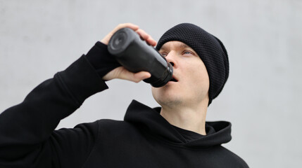 Male runner drinking water from a black plastic bottle after a cardio workout. Sportsman in black...