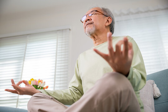 Asian Old Man Practise Yoga And Meditation In Lotus Position And Closed Eyes, Lifestyle Senior Man Lotus Pose Doing Yoga For Mental Balance Breathing Air Relaxing On Sofa At Home, Healthy Life Habits