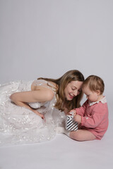 White European young woman with blonde hair in a white dress with a small child in a pink suit with a gift in her hands isolated on white background