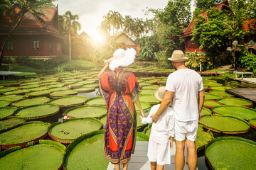 Back view of traveling family looking at beautiful pond with giant lotus flowers. Tropical island....