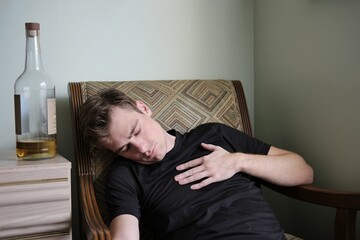 Obraz premium young man sleeping in an armchair near a bottle of alcohol