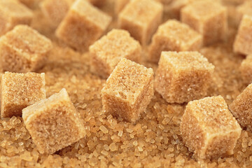 Brown sugar cubes on cane sugar crystals, close up. Demerara golden sugar.
